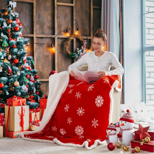 mujer blanca sentada en un sofa cubriendo sus piernas con una manta roja y a un costado un arbol de navidad