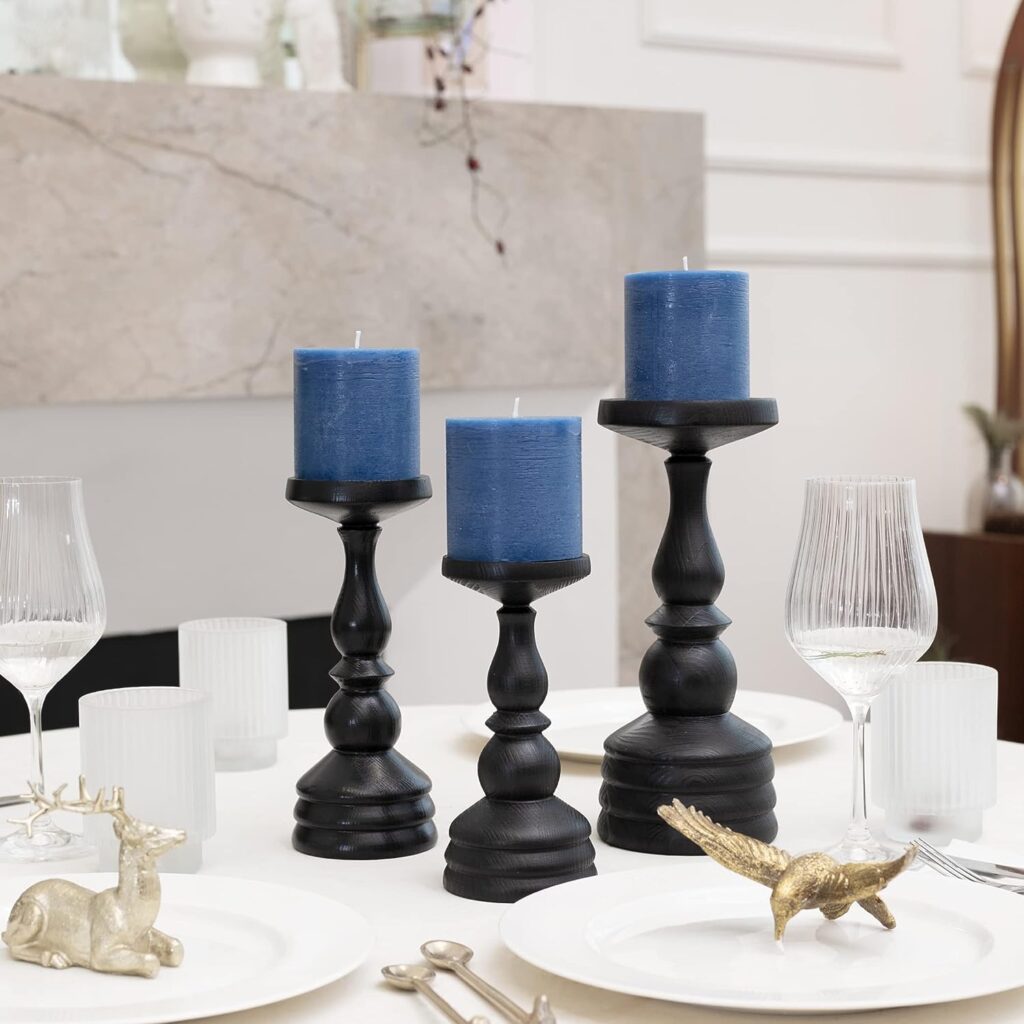 tres velas con base color negro encima de una mesa con adornos de animales dorados encima de platos blancos y vasos de cristal