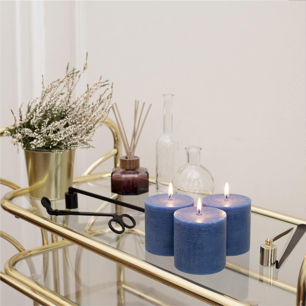 tres velas azules encendidas encima de una mesa de vidrio con orillas doradas y un adorno de ramas verdes