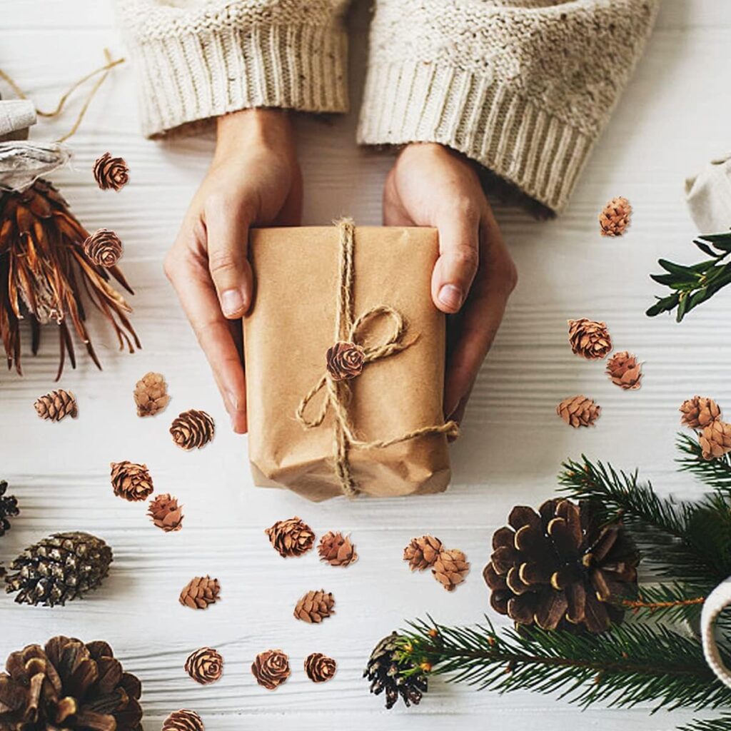 un par de manos sosteniendo una caja de regalo cafe y en la mesa varias piñas navideñas cafes de diferentes tamaños